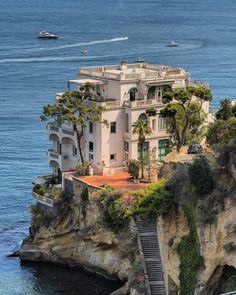 an image of a house on top of a cliff by the ocean with stairs leading up to it