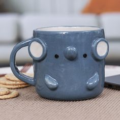 a blue mug with two faces on it sitting next to crackers and a laptop