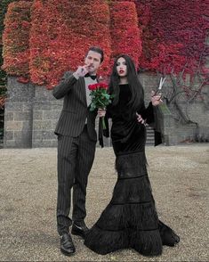 a man and woman dressed in black standing next to each other with flowers on their hands