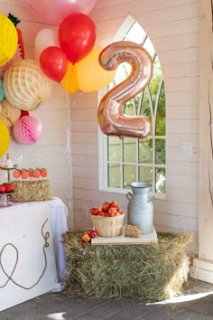 a table topped with lots of balloons next to a number 2 sign and hay bales