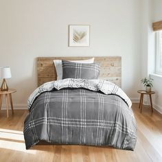 a bedroom with wood floors and white walls, has a gray plaid comforter on the bed