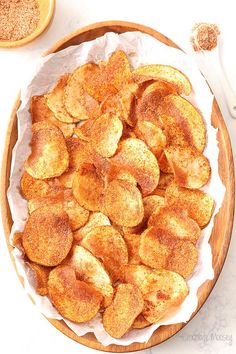 a wooden bowl filled with fried potatoes on top of a white table next to a spoon