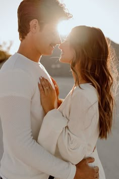 a man and woman standing next to each other in front of the sun with their faces close together