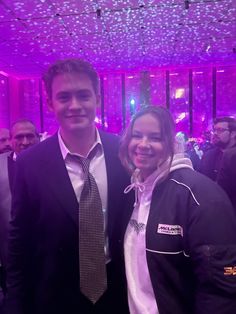 a man and woman standing next to each other in front of a purple lit room