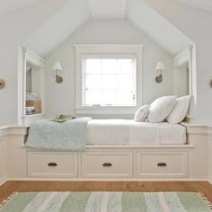 a bed sitting under a window in a bedroom next to a white dresser and rug