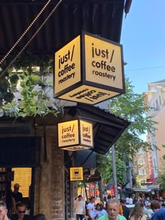 people are walking down the sidewalk in front of a coffee shop with lights hanging from it's roof