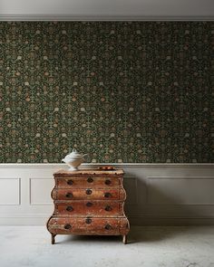 an old dresser in front of a wallpapered room