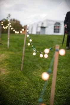 string lights strung from poles in the grass with a man standing next to them behind