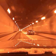 two cars driving down a tunnel in the dark with orange light coming from behind them