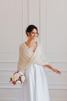 a woman in a white dress holding a bouquet and wearing a shawl over her shoulders