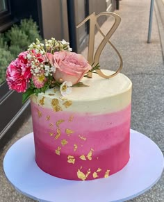 a pink and gold ombretta cake with flowers on the top sitting on a white plate