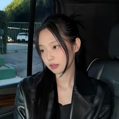 a woman sitting in the back seat of a car wearing a leather jacket and looking at the camera