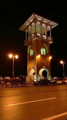 a tall clock tower sitting on the side of a road next to street lamps and parked cars