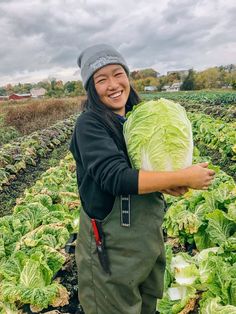 a woman is holding a large cabbage in her hands and smiling at the camera while standing in a field