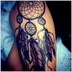 a woman's thigh with a tattoo on it that has an image of a dream catcher and feathers