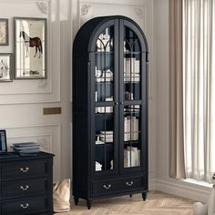 a tall black bookcase with glass doors in a living room next to a window