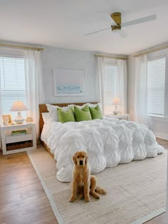 a dog sitting on the floor in front of a bed with white sheets and pillows