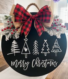 a merry christmas sign with pine trees and plaid bow hanging from it's side