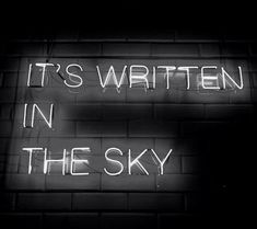 it's written in the sky neon sign on a brick wall with white writing