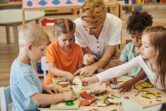 a woman sitting at a table with children in front of her and making crafts on the table