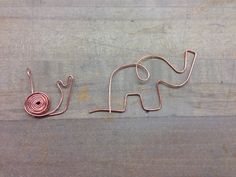 a wire sculpture of an elephant with a snail on it's back sitting on a wooden surface