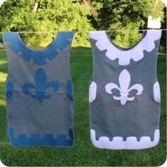 two baby bibs hanging on a clothesline in the grass with trees in the background