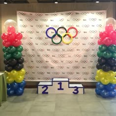 balloon columns in front of a wall with the olympic symbol on it and balloons around them