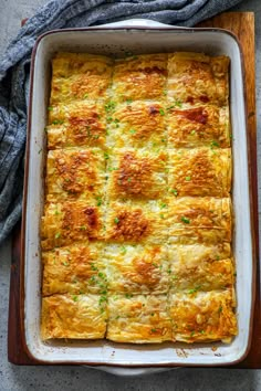 a casserole dish with meat and cheese in it on a wooden tray next to a gray towel