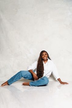 a young woman sitting on the ground with her legs crossed and smiling at the camera