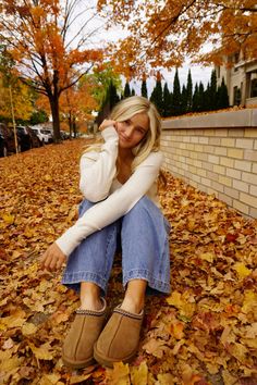 a woman is sitting on the ground with her feet up and wearing slippers in front of fall leaves