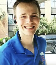 a man wearing a headset smiles at the camera while standing in front of a building