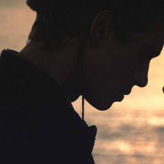 a man holding a cell phone to his ear with the sun setting in the background