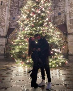 a man and woman standing in front of a large christmas tree with lights on it