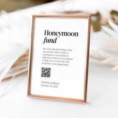 a sign that reads honeymoon find next to some white feathers on a table with a gold frame