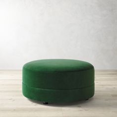 a green ottoman sitting on top of a hard wood floor next to a white wall