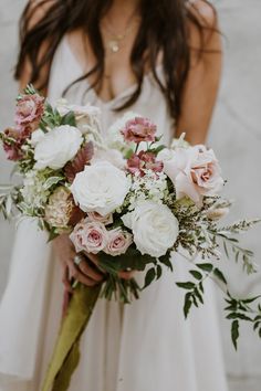 a woman holding a bouquet of white and pink flowers with greenery in her hands