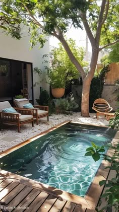 a small pool in the middle of a backyard with chairs and tables around it, surrounded by greenery