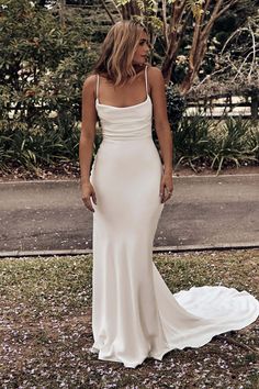 a woman wearing a white dress standing in the grass with her back to the camera