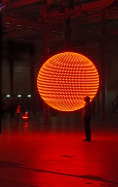 a man standing in front of a large ball with red lights on it's sides