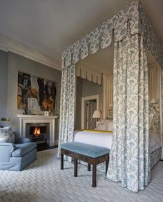 a bedroom with a four poster bed, blue chair and fireplace