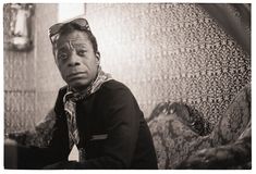 a black and white photo of a man with sunglasses on his head sitting in front of a wall