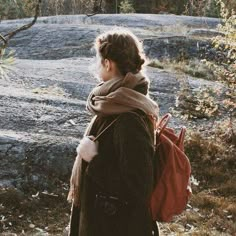 a woman with a red bag is standing in front of some rocks and trees looking at something