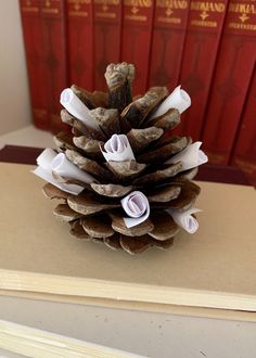 a pine cone made out of paper sitting on top of a book shelf next to red books