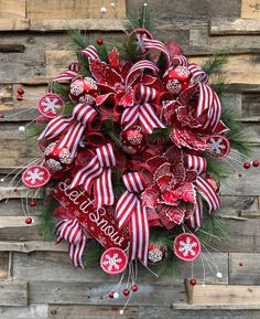 a christmas wreath with red and white ribbons on it, hanging from a wooden wall