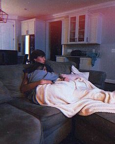 a man laying on top of a couch next to a woman under a blanket in a living room