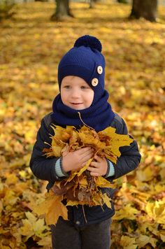 a young boy in a blue hat holding leaves