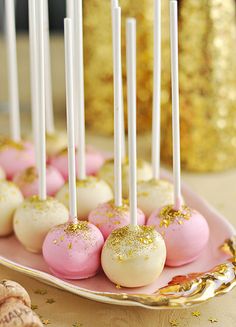 pink and white cake pops with gold sprinkles are on a platter