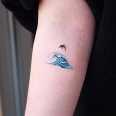 a person with a tattoo on their arm has a blue wave in the water and a black bird flying over it