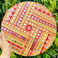 a person holding up a colorful plate in front of some trees and grass with their hand on it