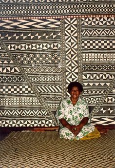 a woman sitting on top of a bed in front of a wall with geometric designs